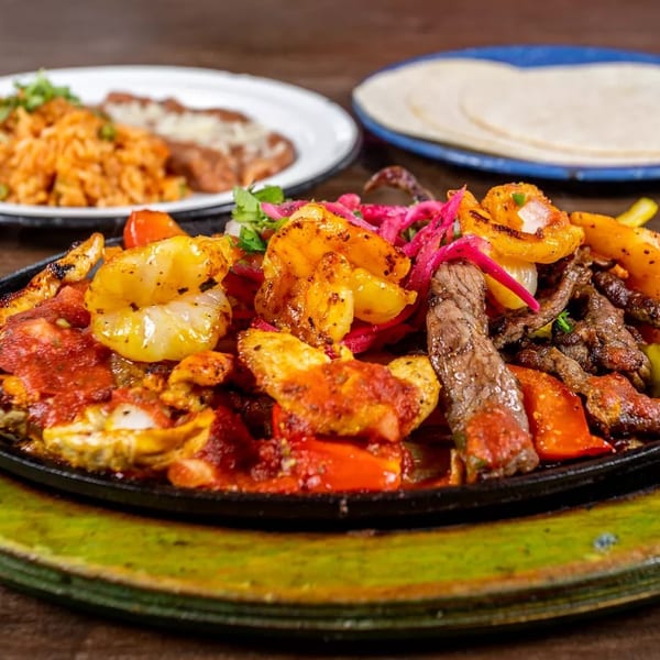Sizzling fajitas with shrimp, steak, chicken, peppers, and onions, served with rice and tortillas.