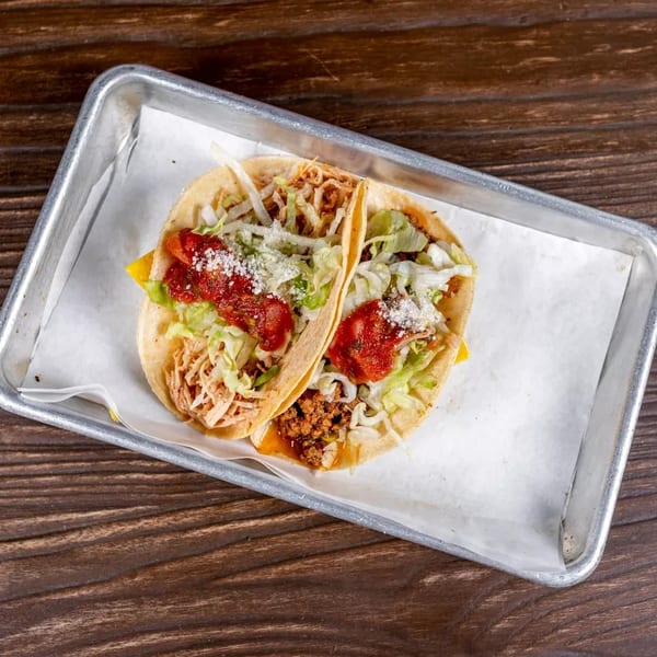 Two tacos, one with shredded chicken and the other with ground beef, in a metal tray.