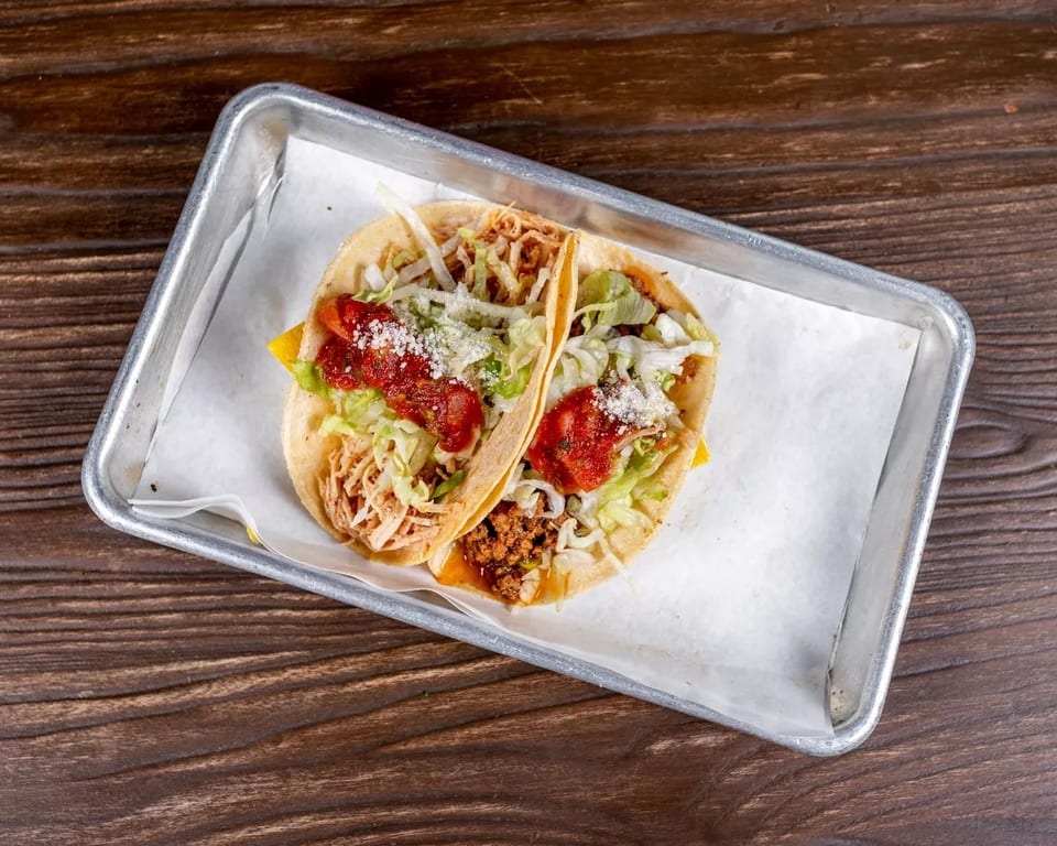 Two tacos, one with shredded chicken and the other with ground beef, in a metal tray.