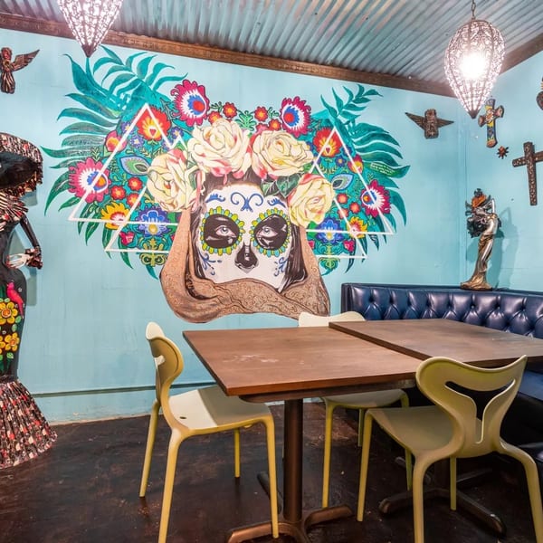 Restaurant interior with a vibrant Day of the Dead mural, blue booth, and light green chairs.