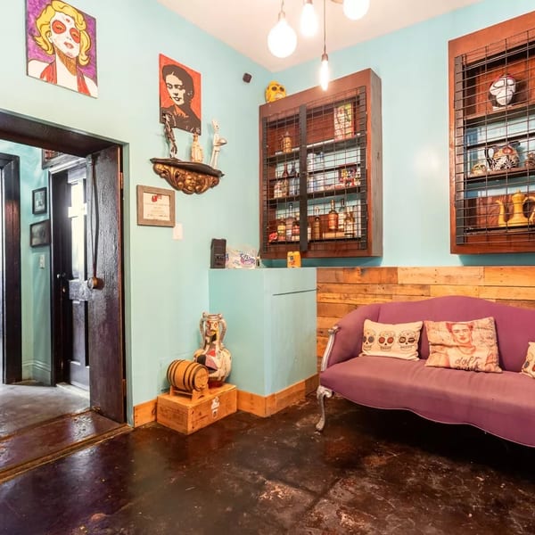 Eclectic restaurant interior with a purple couch, wooden accents, and vibrant artwork on light blue walls.