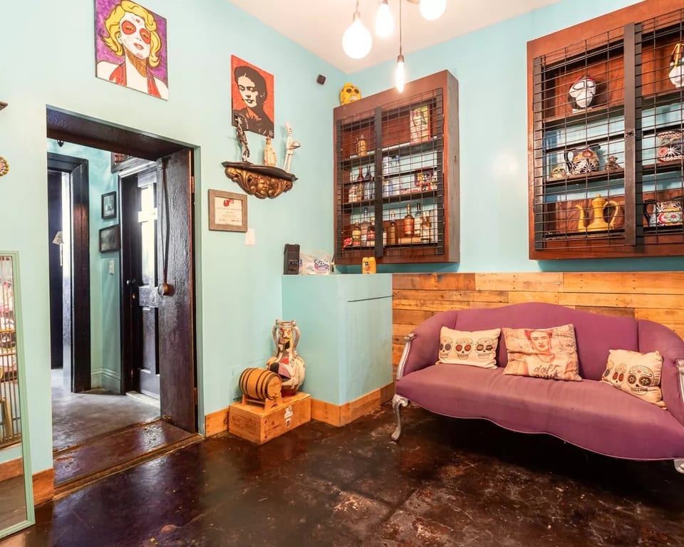 Eclectic restaurant interior with a purple couch, wooden accents, and vibrant artwork on light blue walls.